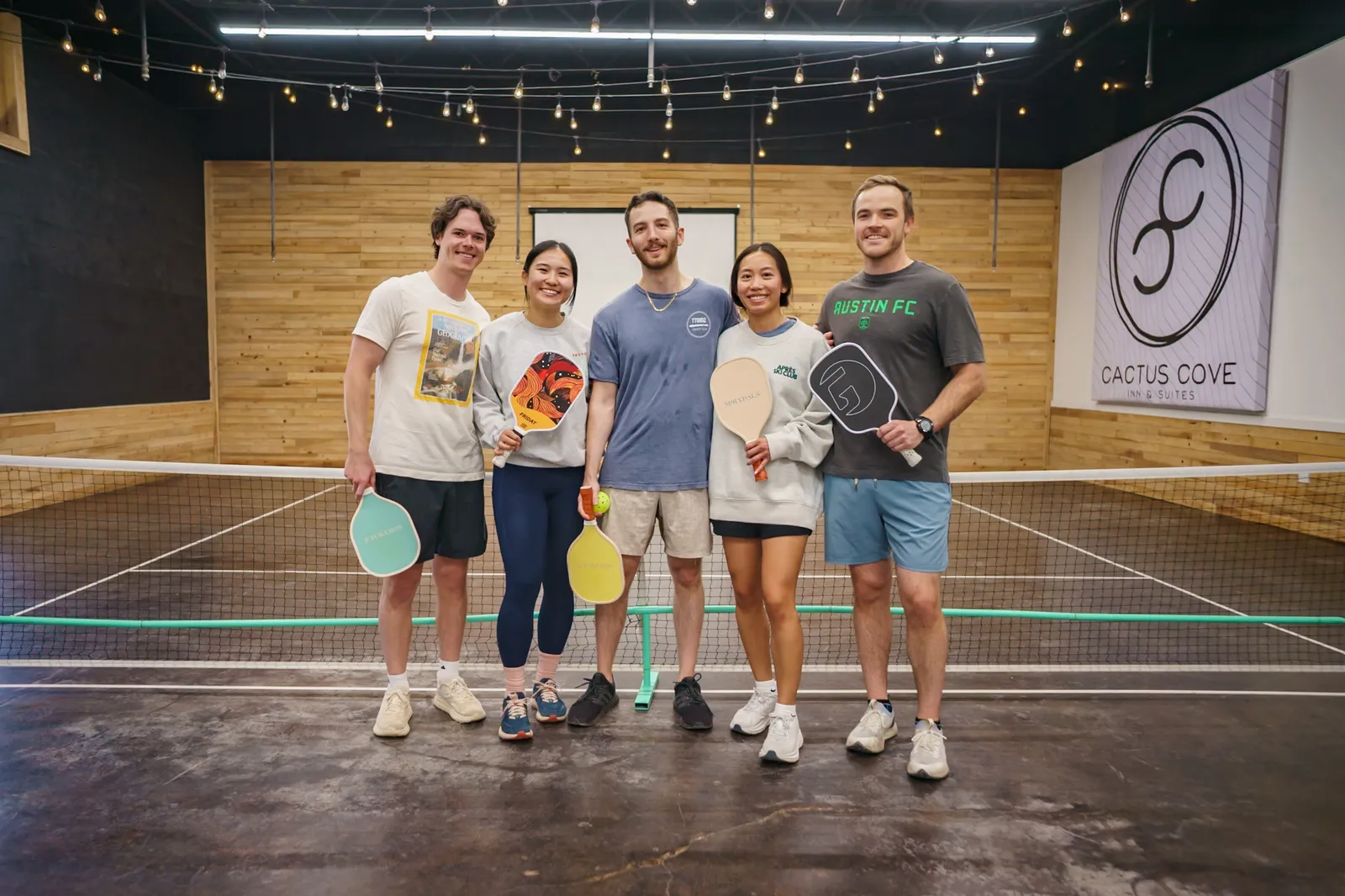 Friends posing with paddles on the indoor pickleball court