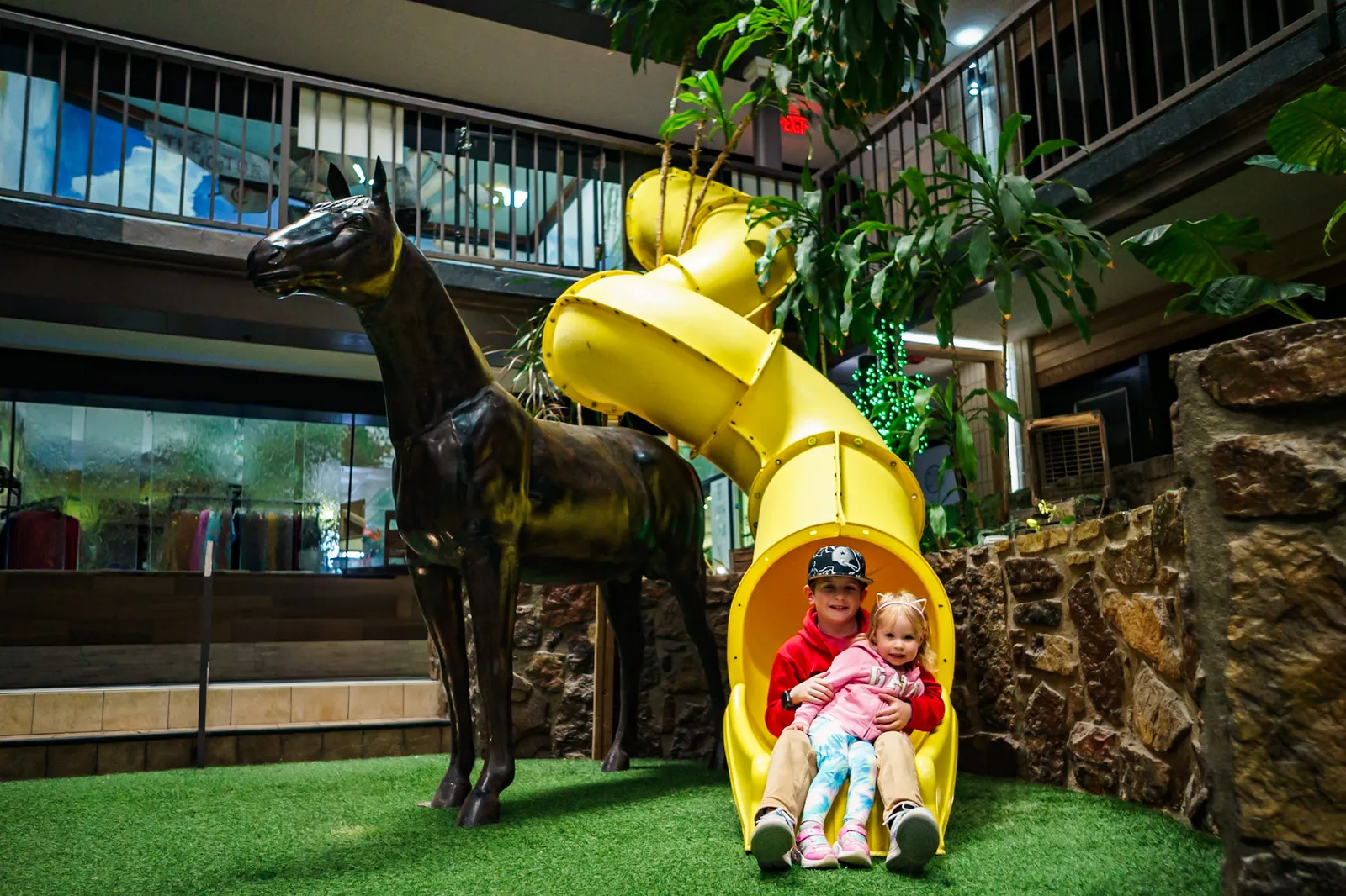 Two kids arriving at the bottom of the yellow indoor slide