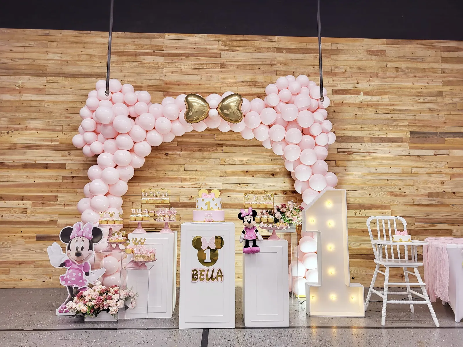 A Minnie Mouse first-birthday party setup with a pink balloon arch